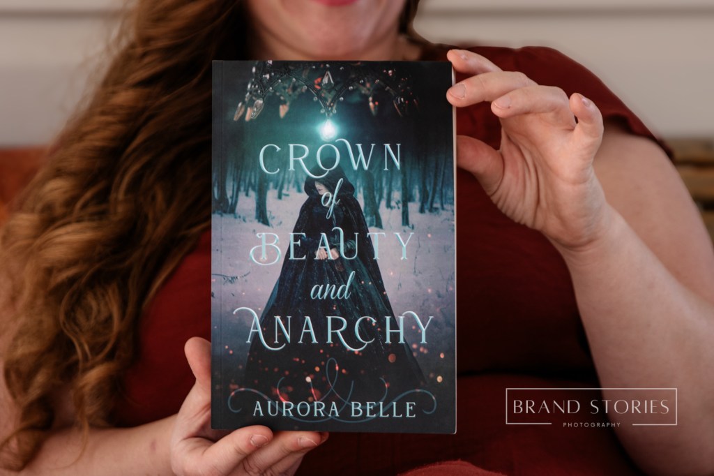 Girl holding a Book called Crown of Beauty and Anarchy by Aurora Belle